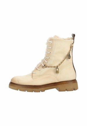 Beige suède veterboot met dikke bruine zool, een harige binnenkant en een gouden ketting met hangslotbedel aan de zijkant.