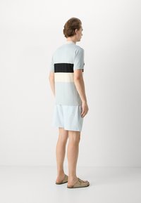 Polo de mangas curtas em azul claro com riscas horizontais em preto, branco e creme, combinado com calções listrados em azul claro e branco.