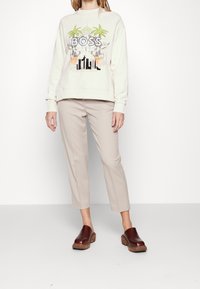 Krémová mikina s grafikou "BOSS", design palmy; světle krémové úzké kalhoty; tmavě hnědé dřeváky s dřevěnými podrážkami.