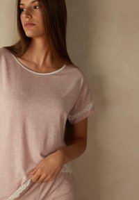 Roze t-shirt met korte mouwen van een zachte stof met een ronde halslijn, voorzien van witte kantaccenten op de mouwen en de zoom. Glad textuur.