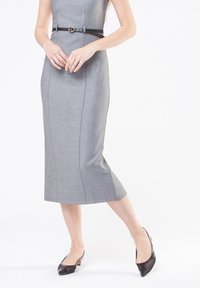 Abito grigio aderente con una cintura in vita, caratterizzato da una texture liscia e un orlo al ginocchio. Indossato con tacchi in pelle verniciata nera.