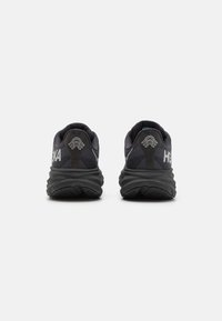 Des chaussures de course noires avec une tige en maille texturée, une semelle rembourrée et un logo HOKA distinctif sur le talon et le côté.
