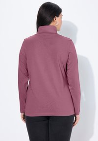 Langärmeliges Rollkragenshirt in Mauve, aus weichem Stoff. Es hat eine schlanke Passform und einen hohen Kragen, kombiniert mit dunklen Hosen.