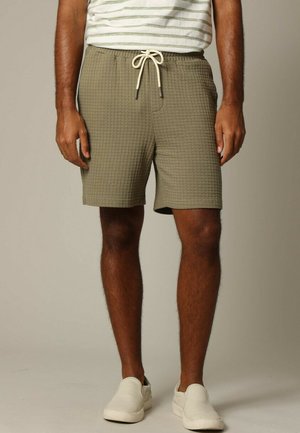 Shorts vert olive avec un design texturé, semblable à un gaufre. Comprend une taille élastique avec un cordon de serrage, des poches latérales et une coupe décontractée.