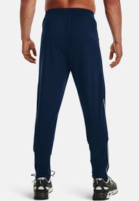 Marina atletiska byxor med elastiskt midjeband, sidostråk och rak skärning. Slätt tyg, bärs med svarta och vita sneakers.