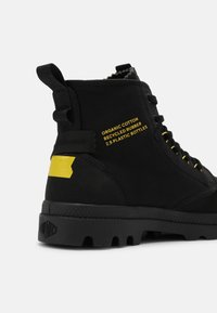 Bottes montantes noires fabriquées en coton biologique et en caoutchouc recyclé. Présentent des accents jaunes, un marquage marqué et une semelle texturée avec un motif à crampons.