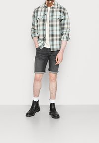 Vaaleansininen, musta ja valkoinen ruudullinen flanellipaita, jonka alla on vaaleancreme t-paita. Tummat denimmishortsit, joiden lahkeet on käännetty, sekä mustat nilkkasaappaat.