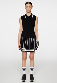 Black sleeveless polo dress with white stripes, zip closure at the neck, and a flared skirt; worn with black shoes and patterned white socks.
