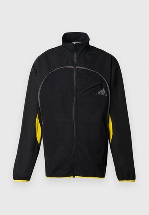 Veste de sport noire avec des accents jaunes sur les côtés. Comprend un col haut, une fermeture éclair intégrale et une poche avant. Fabriquée en tissu texturé.