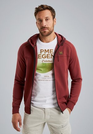 Maroon zip-up hooded sweatshirt, soft fabric, featuring a white graphic t-shirt underneath with green and gold text, worn with light cargo shorts.
