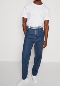 Vit t-shirt ihop med blå denimjeans med ett märkesbälte. Jeansen har rak passform och en klassisk femficksdesign.