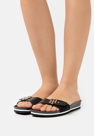 Sandalias deslizantes negras con un upper de cuero texturizado, que presentan un acento dorado brillante y una suela con rayas blancas. Diseño ligero y cómodo.