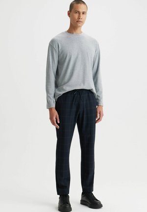 Szara koszula z długim rękawem w połączeniu z ciemnoniebieskimi spodniami w kratę; spodnie mają elastyczny pas z troczkami; czarne sneakersy dopełniają outfit.