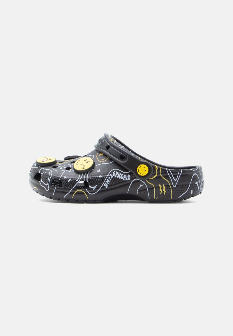 Chaussure noire de style croc avec des accents visage souriant jaune ; présente un design à motifs de lignes blanches et de graphiques, fabriquée en matériau léger.