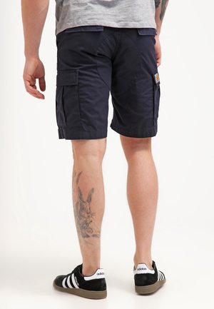 Pantaloncini cargo blu navy con tasche laterali, realizzati in tessuto resistente. Presentano un'etichetta sul lato sinistro e cuciture laterali. Scarpe da ginnastica nere e bianche visibili.