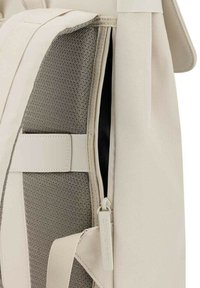 Zaino in tela beige con interno grigio strutturato, chiusura con zip e tracolla liscia. Design minimalista con una finitura morbida.