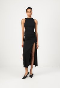 Melna bezpiedurkņu kleita ar sānu izgriezumu un drapējumiem, izgatavota no gludas materiāla. Saskaņota ar melniem smailajiem papēžiem un gaiši rozā somu.