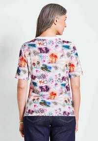 Korte mouwen shirt met een multikleurig tropisch patroon van palmbomen, harten en bloemdessins op een lichte achtergrond.