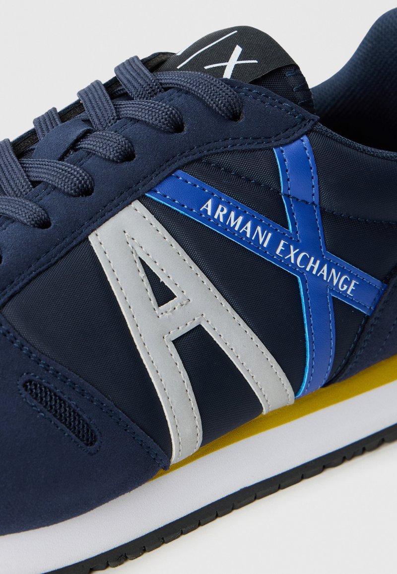 Zapatillas náuticas de color marino que combinan materiales de tela y sintéticos, con un logo en gris y azul, una mediasuela blanca y una suela exterior negra texturizada.
