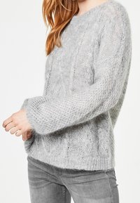 Pull gris clair en maille avec une coupe ample, présentant un motif texturé et des manches larges. Matière douce et duveteuse avec un col décontracté.