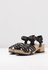 Zwarte leren sandalen met bandjes en een houten blokhak, voorzien van studs en een verstelbare enkelriem. Open teen ontwerp.