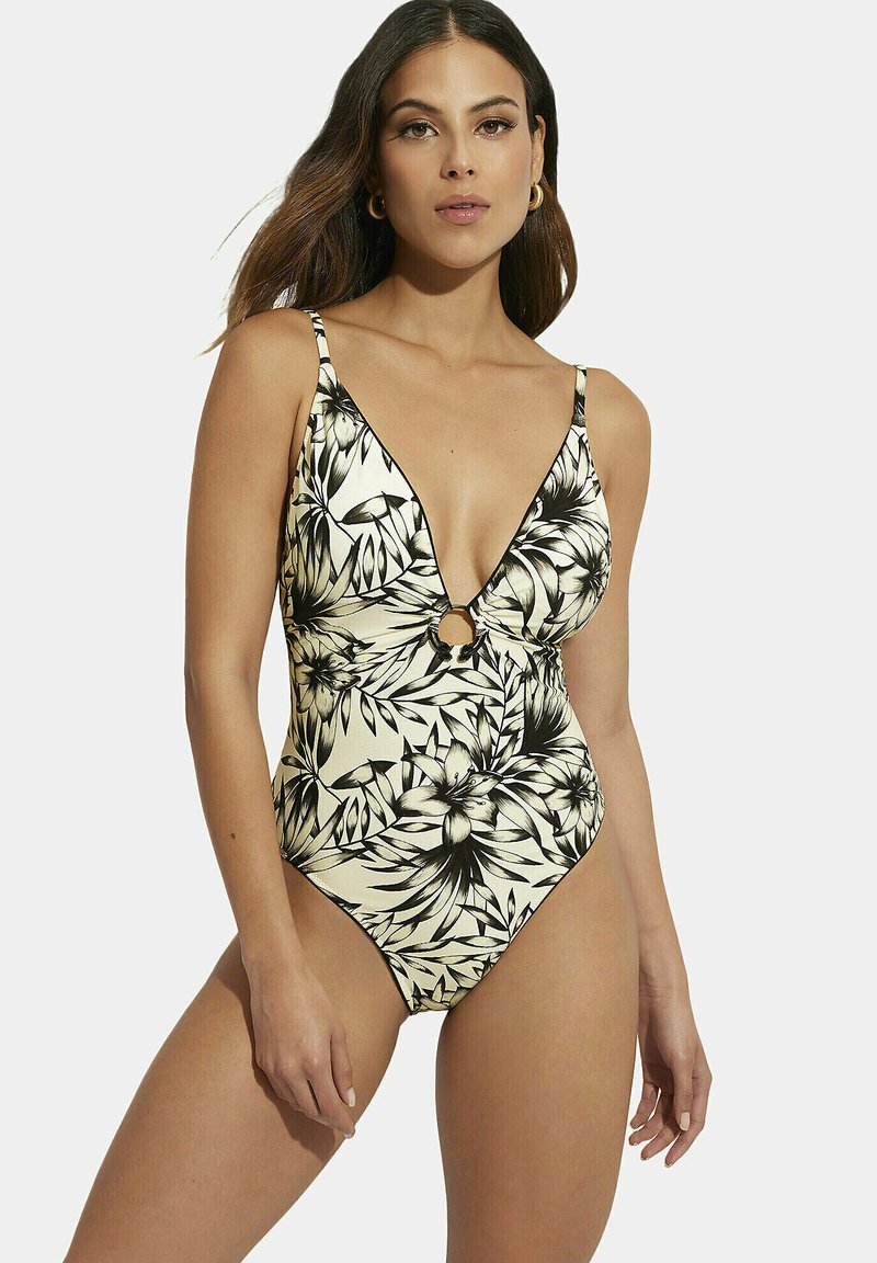 Maillot de bain une pièce de couleur crème avec un motif floral noir, présentant des bretelles réglables, un décolleté en V profond et un détail en forme de cercle.