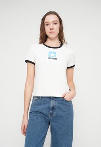 Λευκό βαμβακερό T-shirt με μαύρο ριγέ λαιμόκοψη και μανίκια, με μπλε λογότυπο αστεριού και κείμενο "CONVERSE" στο μπροστινό μέρος.