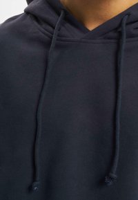 Felpa blu navy con scollo a V, cappuccio concordini e tessuto texture. Presenta lunghi cordini piatta con accenti a nodo.