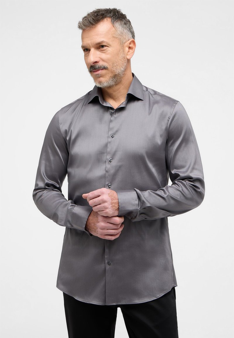 Grijs, langemouwen shirt van een gladde, glanzende stof met een klassieke kraag, knoopsluiting en een gebogen zoom. G gedragen met zwarte broek.