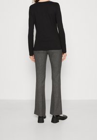 Schwarzes langärmliges Oberteil kombiniert mit taillierten grauen gemusterten Hosen. Das Outfit hat einen schmalen Schnitt und standardmäßige Ärmellängen, ergänzt durch schwarze Absatzschuhe.