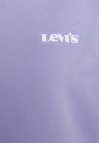 Camiseta de algodón de color púrpura claro con un logo rectangular blanco de Levi's. La tela tiene una textura suave con un patrón acanalado.