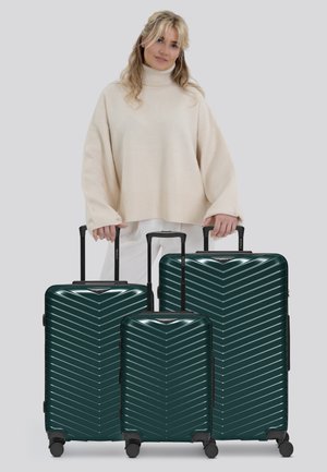 Trois valises rigides légères, de couleur vert foncé, avec un motif en chevron, de tailles variées et dotées de poignées rétractables, sur des roues lisses.
