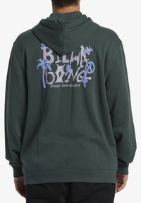 Sudadera de color verde oscuro con un ajuste relajado. Presenta un estampado gráfico en la parte posterior con palmeras, flores y texto en azul claro y blanco.