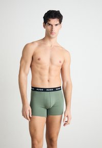 Grüne Boxershorts aus glattem Stoff mit einem schwarzen Bund, der den Markennamen trägt. Enganliegendes Design, mittellange Länge bis zur Oberschenkelmitte und ohne sichtbare Muster.