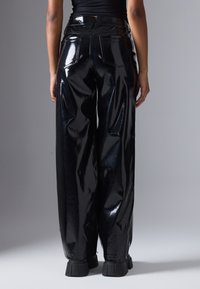 Calças largas de vinil preto brilhante com dois bolsos traseiros e cintura alta. Apresentam uma textura suave e uma superfície refletora brilhante.
