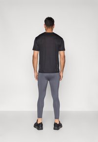 Juoda trumpomis rankovėmis sportinė marškinėliai su šoninėmis siūlėmis, dėvimi su aptempiamomis pilkomis tamprėmis ir juodais batais, matomi iš nugaros.