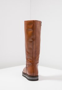 Botte en cuir marron montant jusqu'au genou, avec une texture lisse, un design minimal et une fermeture éclair sur le côté. Présente une semelle robuste avec une légère élévation.