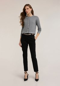 Szary prążkowany sweter z zapięciem na guziki, ozdobiony srebrnymi detalami, zestawiony z czarnymi obcisłymi spodniami i czarnymi butami na wysokim obcasie.