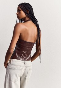 Bruine leren strapless top met een aansluitend ontwerp, gecombineerd met lichte denim jeans. Textuurafwerking op de top, die de slanke silhouet benadrukt.