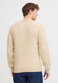 Suéter de punto acanalado beige con mangas largas, cuello redondo y costura texturizada. Corte casual con un material ligeramente elástico.