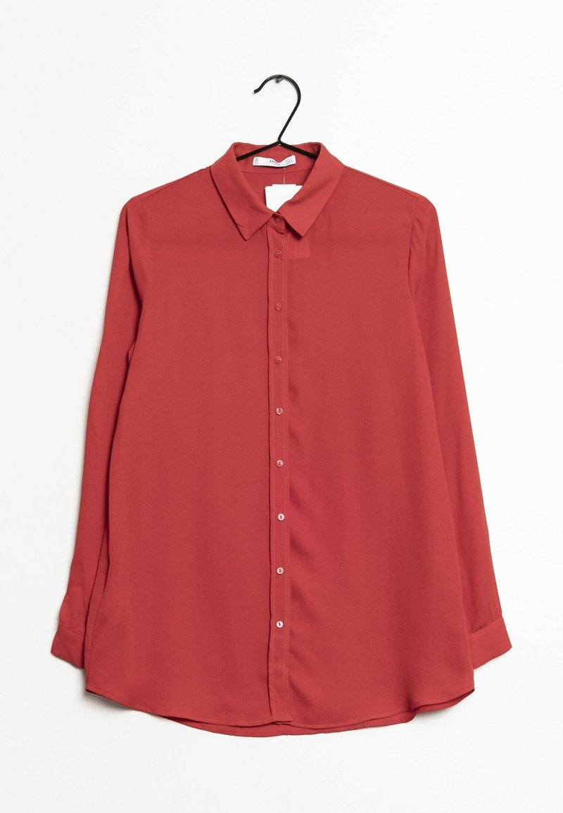 Chemise rouge à manches longues avec col et boutons, suspendue à un cintre noir sur un fond blanc uni.
