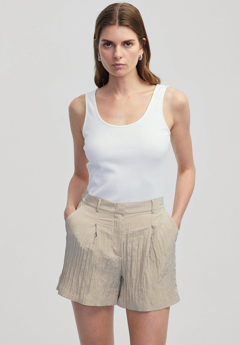 Witte geribde tanktop gecombineerd met lichtbeige geplooide shorts. De shorts beschikken over zijzakken en hebben een gladde textuur.