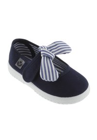 Zapato de lona azul marino con suela de goma blanca, con un lazo de tela a rayas en la parte delantera y un forro interior suave.