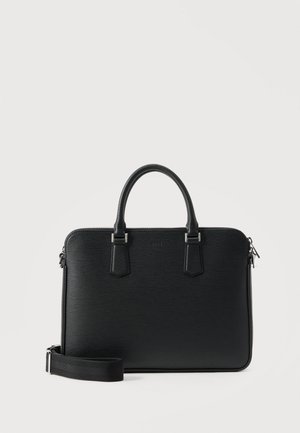 Fekete bőr aktatáska dupla fogantyúval, levehető vállpánttal és cipzáros felső zárral, világos egyszínű háttér előtt.