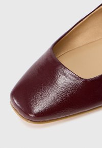 Ballerine in pelle bordeaux con punta quadrata e superficie liscia. L'interno presenta un rivestimento beige e sottili dettagli di cucitura.