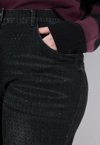 Jeans in denim nero con un motivo testurizzato a pois e un leggero luccichio. Vita media con una tasca standard davanti.