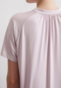 Lichtroze blouse met korte mouwen, gekenmerkt door een gatherende halslijn en een gladde textuur, die subtiele draping aan de achterkant toont.