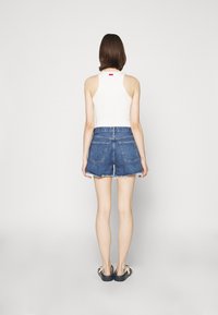 Valkoinen ribattu hihaton paita yhdistettynä korkea vyötäröinen sinisiin farkkushortseihin, joissa on risat reunat ja takataskut, käytetty mustien sandaalien kanssa.