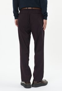 Bordó nadrág testhez álló fazonnal, két háts�ó zsebbel és barna bőr övvel. Sima anyag, enyhe fényességgel; fekete cipővel hordva.