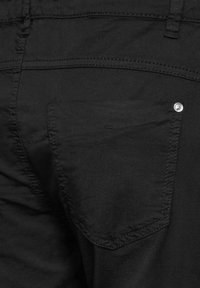 Svarta byxor med en bakficka med en silverknapp. Slät tyg med sömdetaljer som betonar en figursydd passform och en ren design.